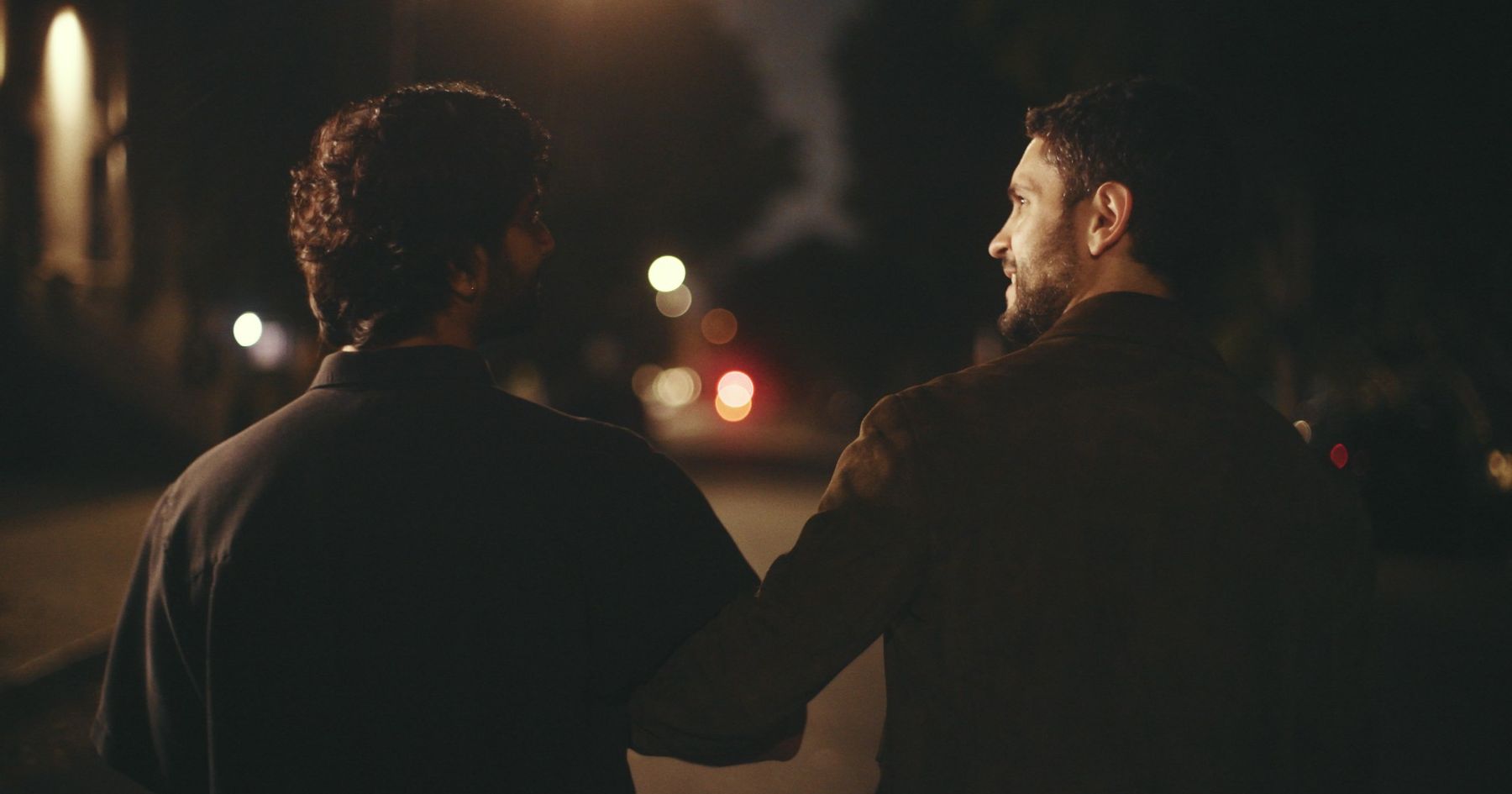 Two men walking side by side down a night street, seen from behind