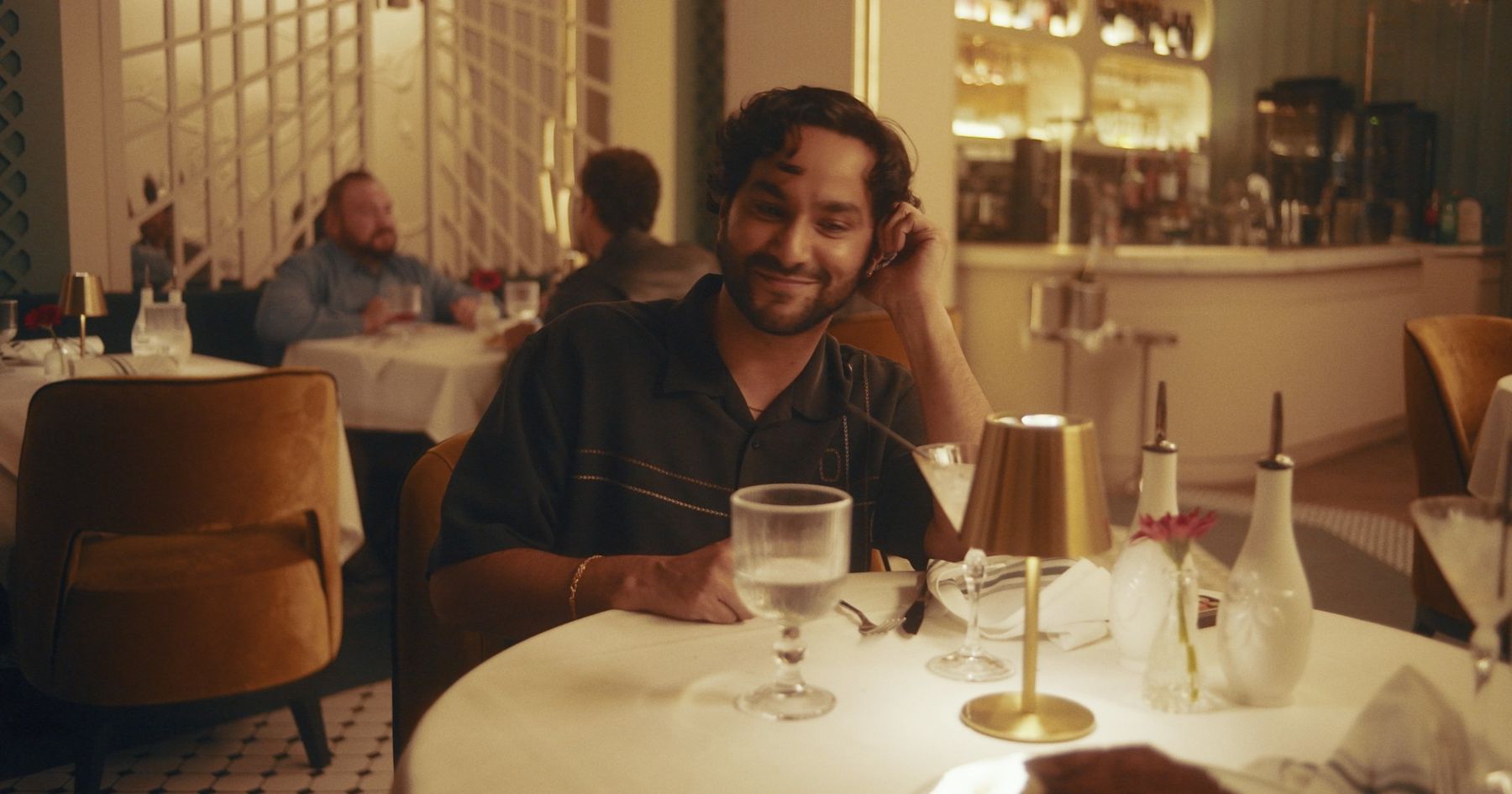 Milo, chin in hand, smiling across a candlelit restaurant table